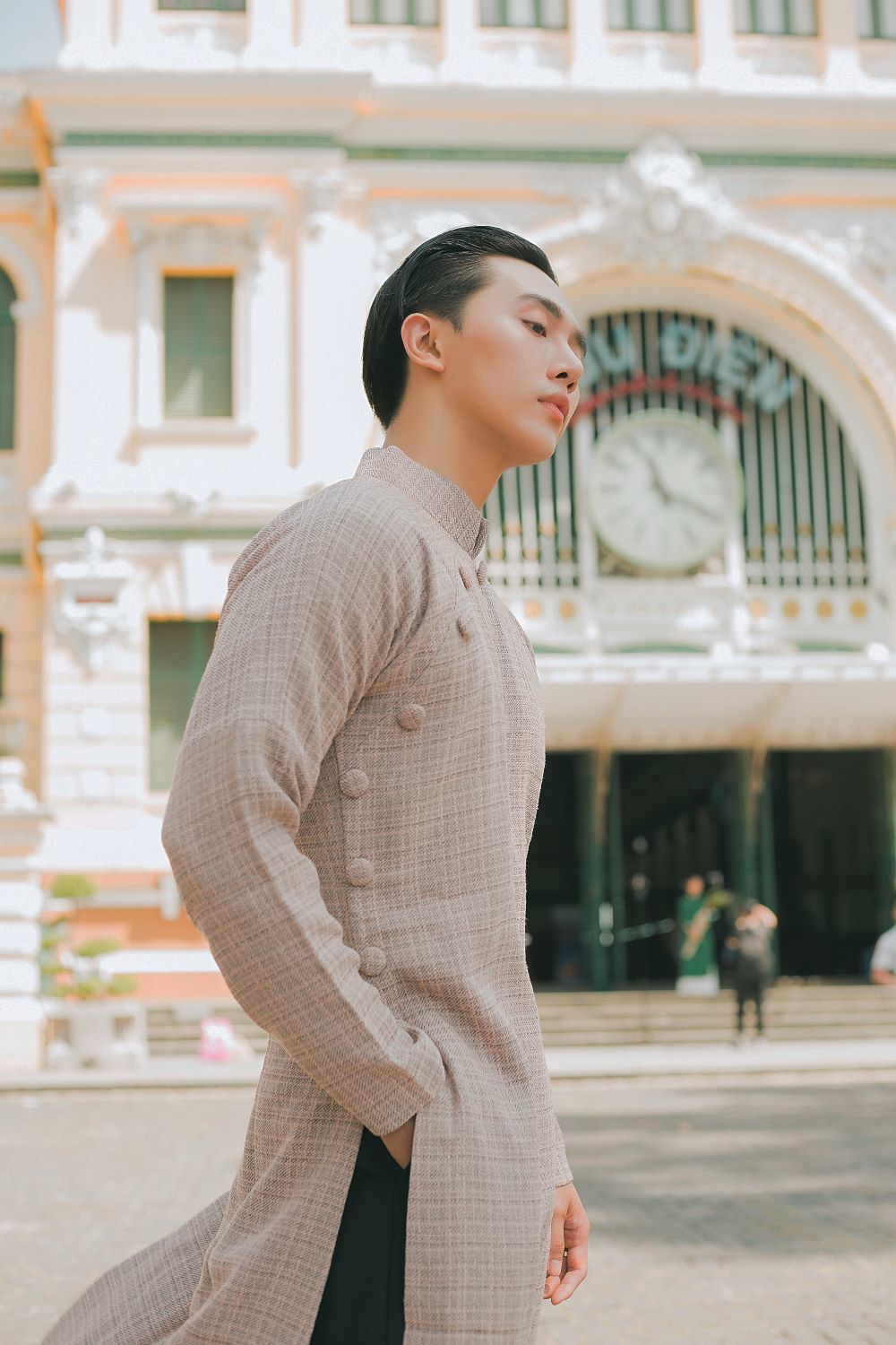 Dương Minh Đăng sải bước cùng tà áo dài màu nâu nhạt trước cổng Bưu điện thành phố.